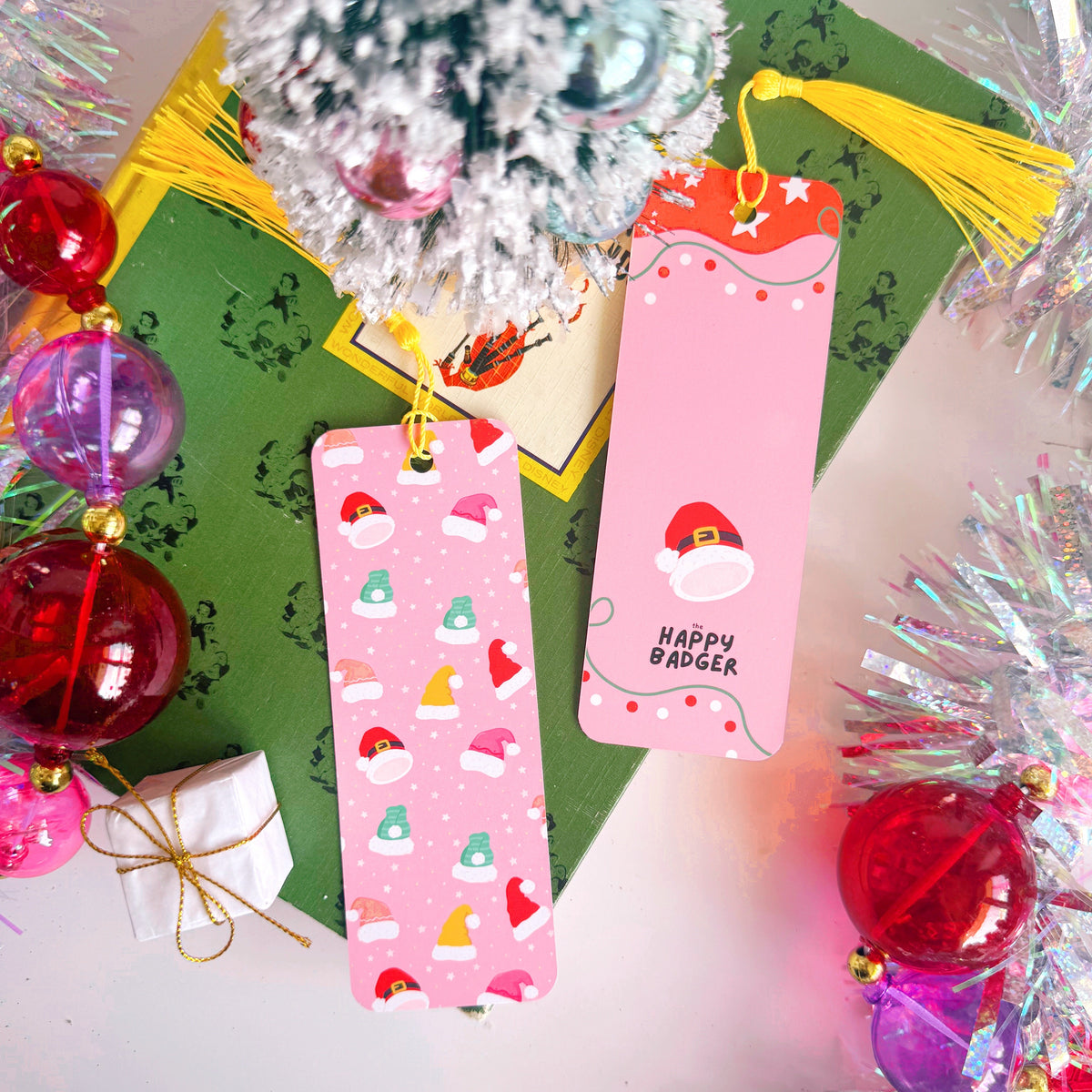 An image showing the front and reverse side of a Christmas bookmark - that has multicoloured Santa and eElf hats on the front, and a festive pattern to the back with the Happy Badger branding logo.