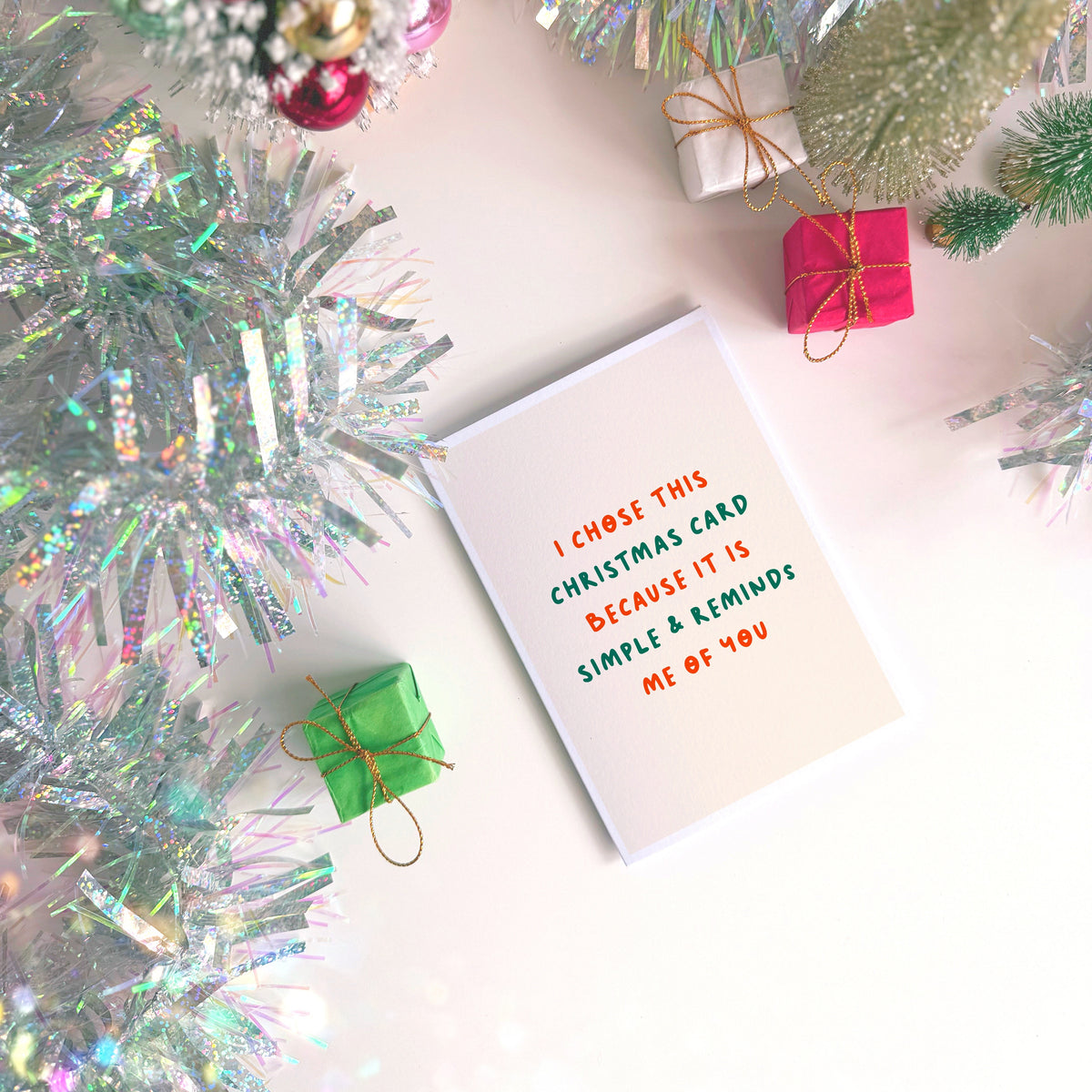 A minimalist Christmas greeting card with a warm cream background and red and green text reading 'I CHOSE THIS CHRISTMAS CARD BECAUSE IT IS SIMPLE & REMINDS ME OF YOU'.