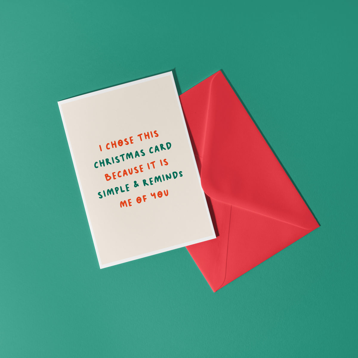 A minimalist Christmas greeting card with a warm cream background and red and green text reading 'I CHOSE THIS CHRISTMAS CARD BECAUSE IT IS SIMPLE & REMINDS ME OF YOU'.