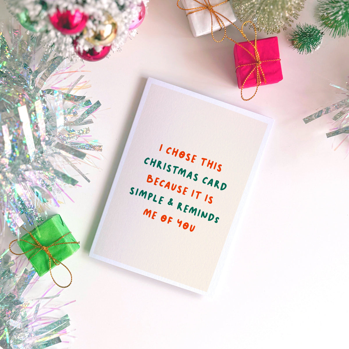 A minimalist Christmas greeting card with a warm cream background and red and green text reading 'I CHOSE THIS CHRISTMAS CARD BECAUSE IT IS SIMPLE & REMINDS ME OF YOU'.
