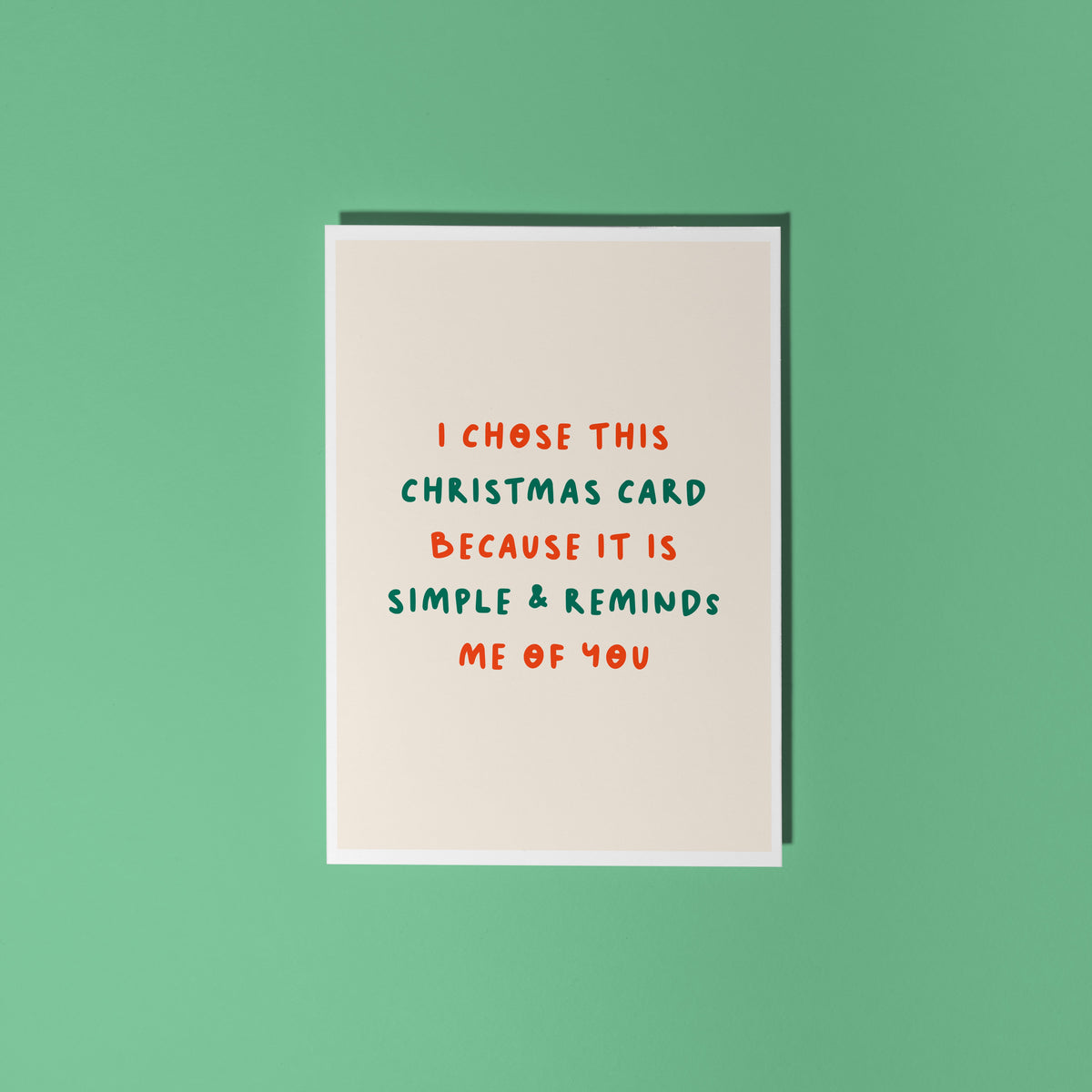 A minimalist Christmas greeting card with a warm cream background and red and green text reading 'I CHOSE THIS CHRISTMAS CARD BECAUSE IT IS SIMPLE & REMINDS ME OF YOU'.