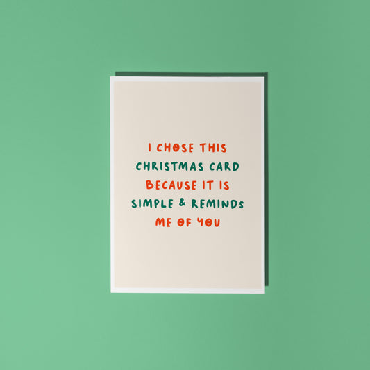 A minimalist Christmas greeting card with a warm cream background and red and green text reading 'I CHOSE THIS CHRISTMAS CARD BECAUSE IT IS SIMPLE & REMINDS ME OF YOU'.