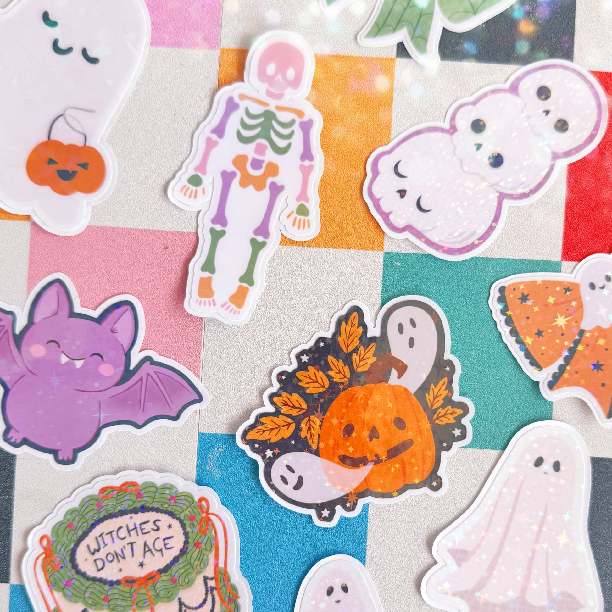 A collection of Halloween-themed die-cut stickers arranged on a pastel checkered background. The stickers feature cute illustrations of ghosts, a skeleton, pumpkins and a bat.