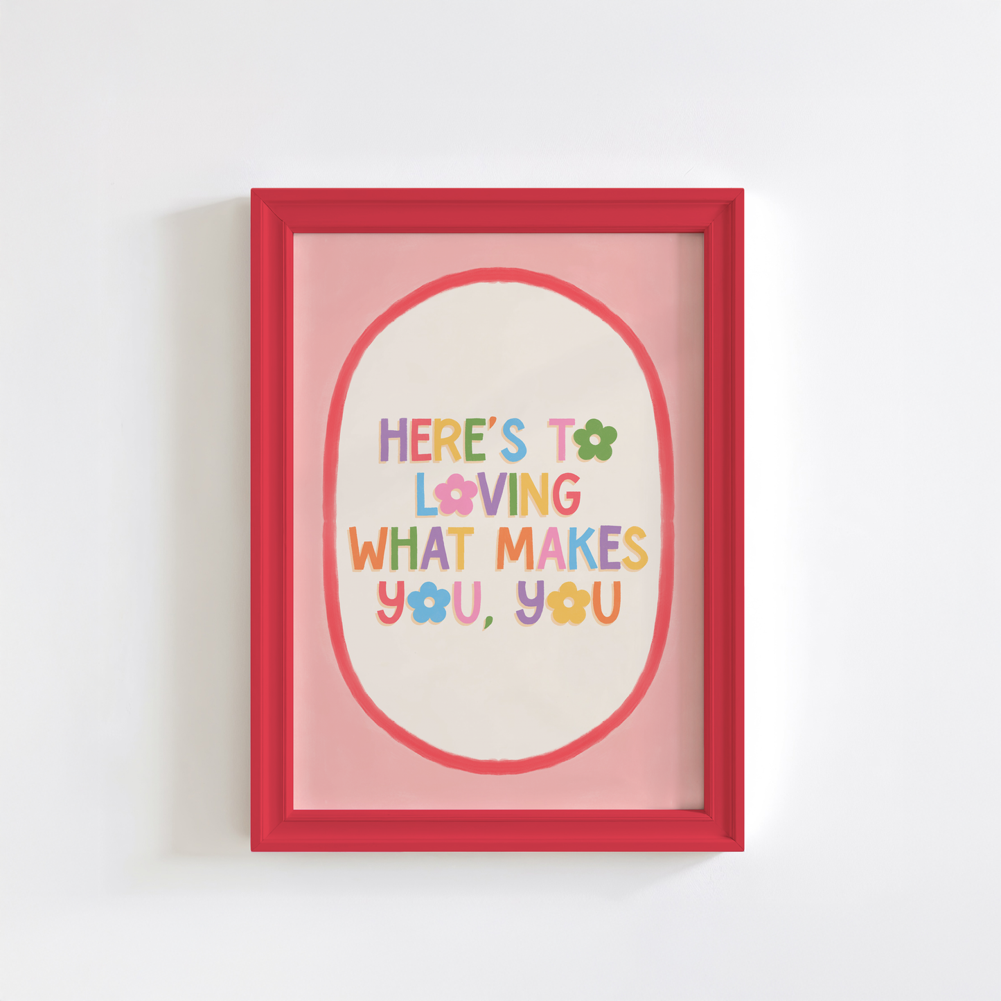A positive quote print that reads 'here's to loving what makes you, you' in multicoloured text with a pink and red oval shaped border.