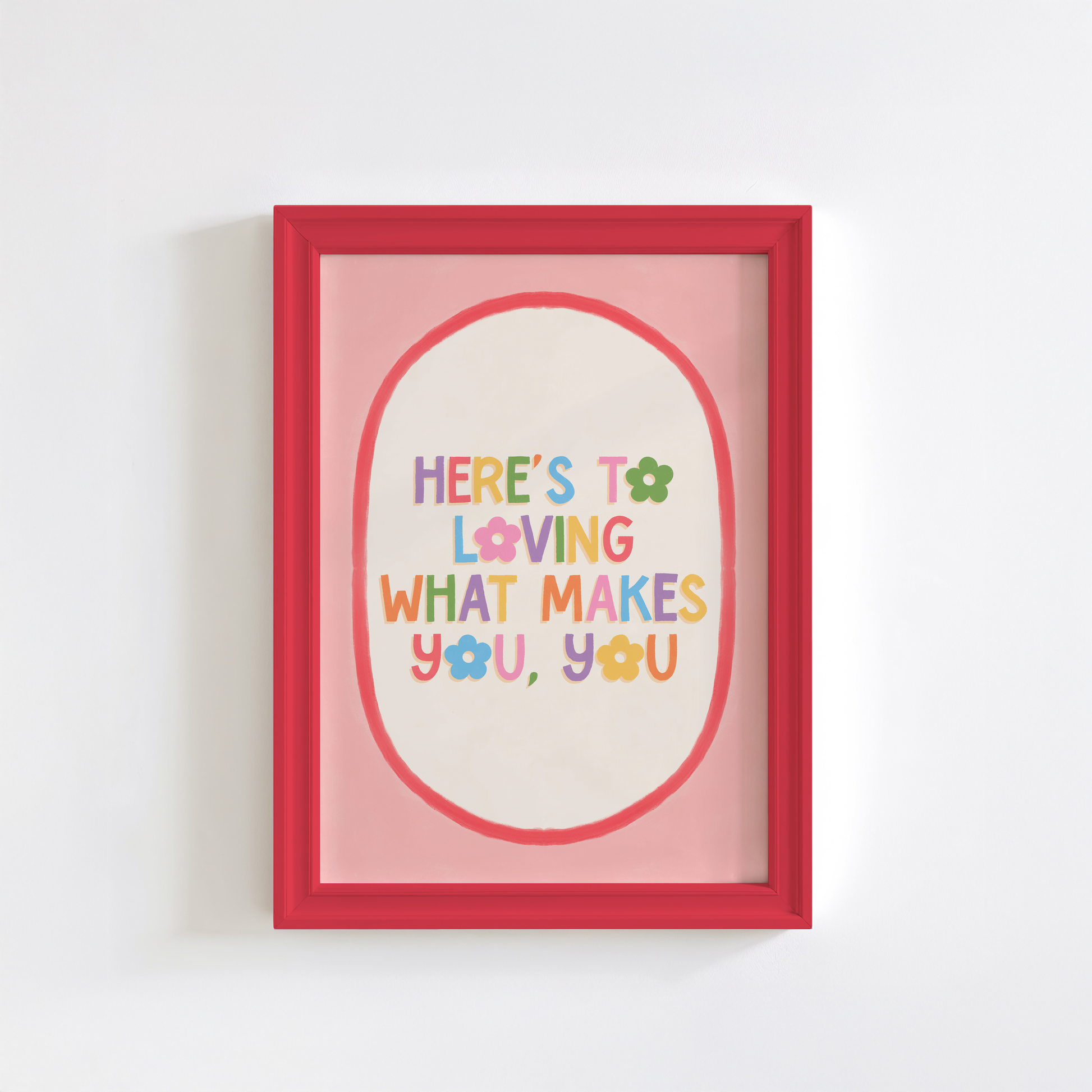 A positive quote print that reads 'here's to loving what makes you, you' in multicoloured text with a pink and red oval shaped border.