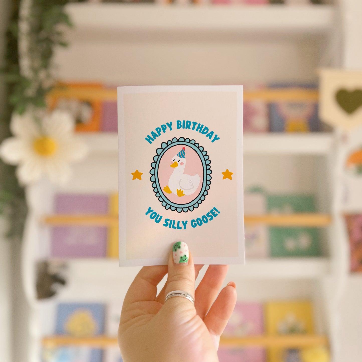 A birthday card with an illustration of a goose in a party hat, with text around it saying 'happy birthday you silly goose'.