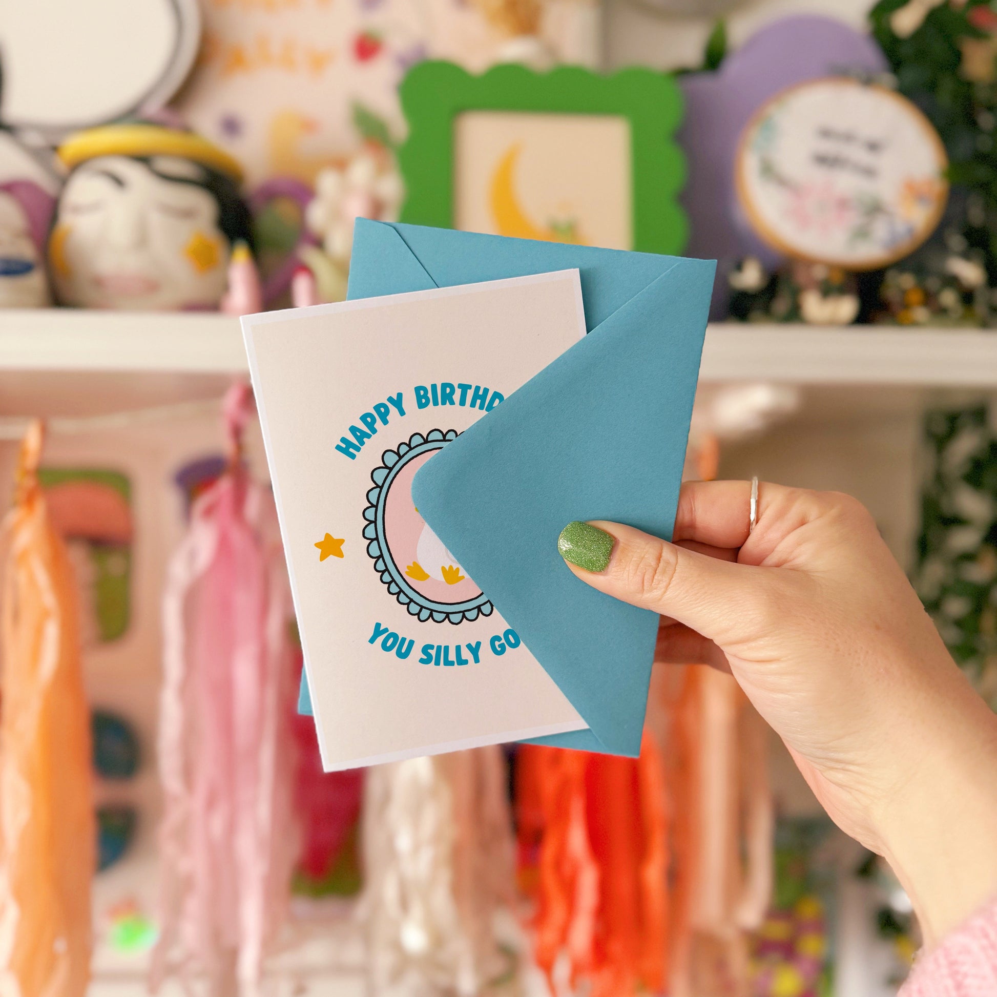 A birthday card with an illustration of a goose in a party hat, with text around it saying 'happy birthday you silly goose'.