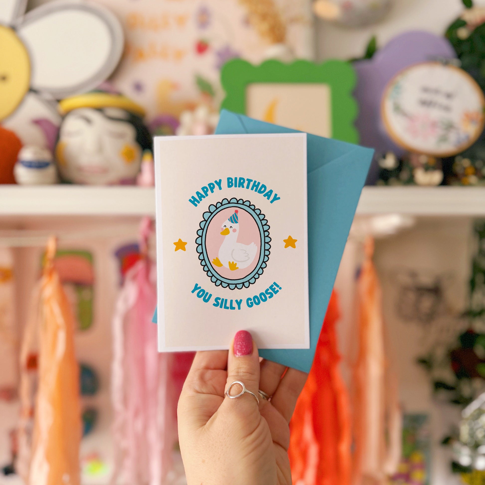 A birthday card with an illustration of a goose in a party hat, with text around it saying 'happy birthday you silly goose'.