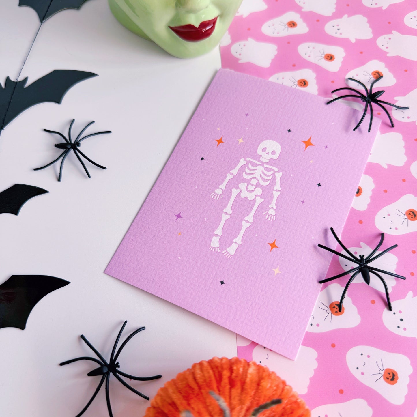 A purple Halloween postcard with an illustration of a skeleton on the front, surrounded by little multi-coloured stars.
