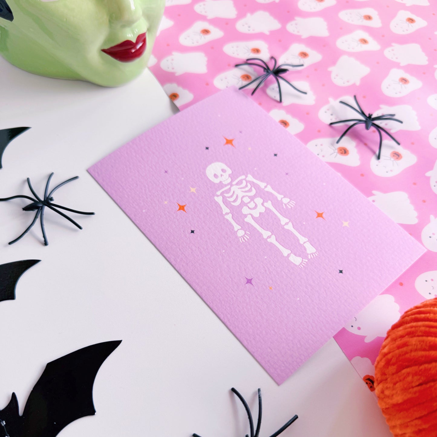 A purple Halloween postcard with an illustration of a skeleton on the front, surrounded by little multi-coloured stars.