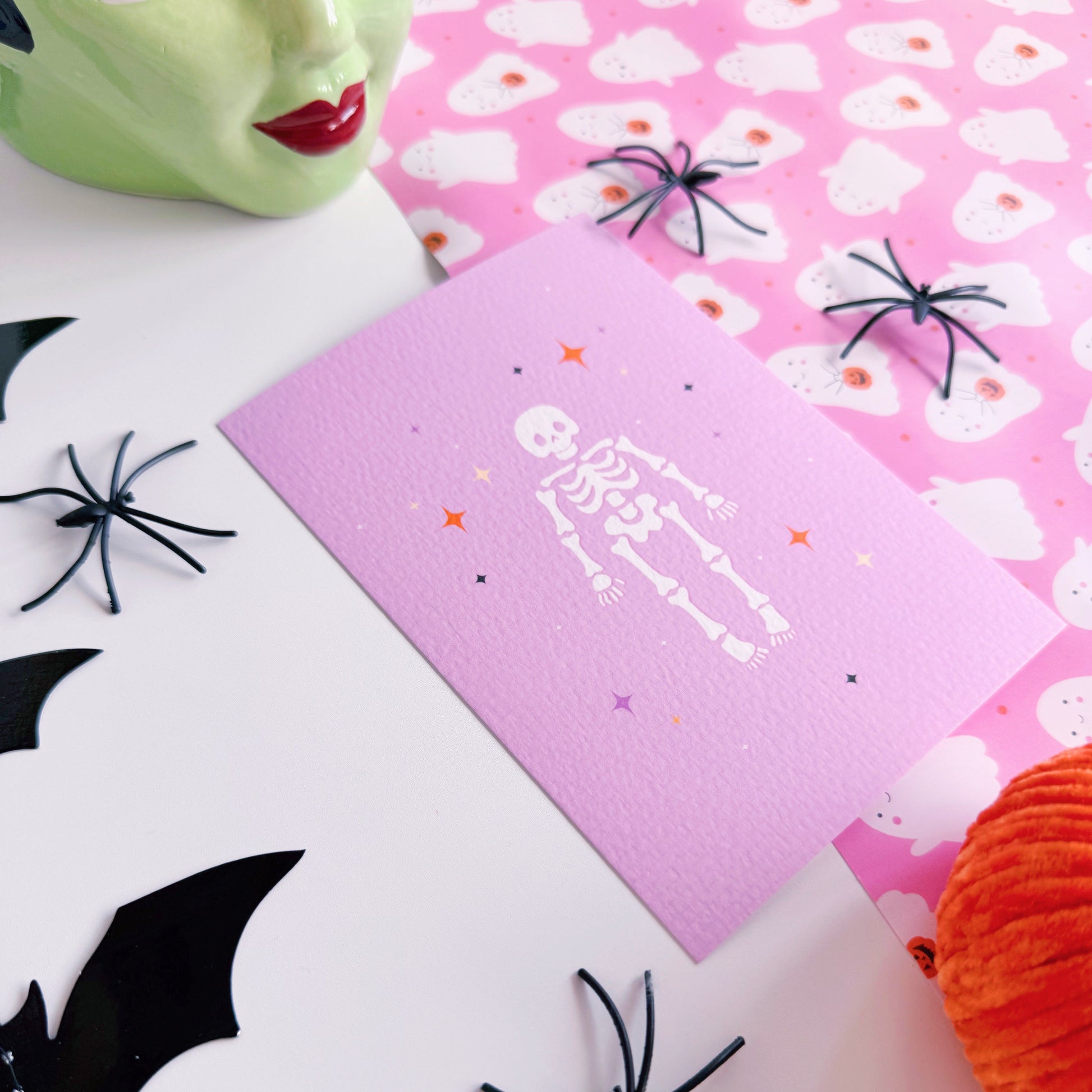 A purple Halloween postcard with an illustration of a skeleton on the front, surrounded by little multi-coloured stars.