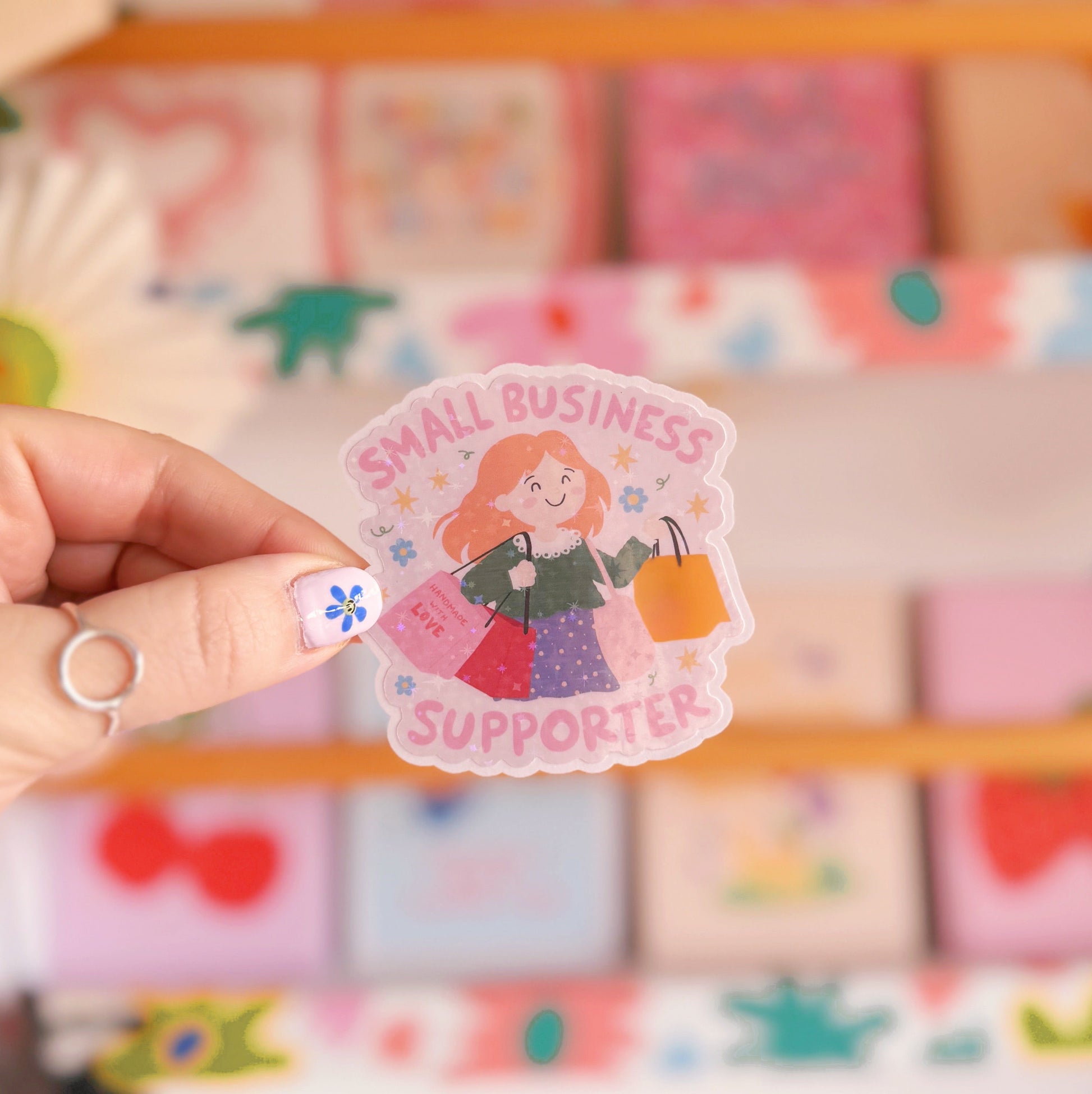 A holographic sticker showing a woman with red hair carrying lots of shopping bags and the words 'small business supporter' around the illustration.