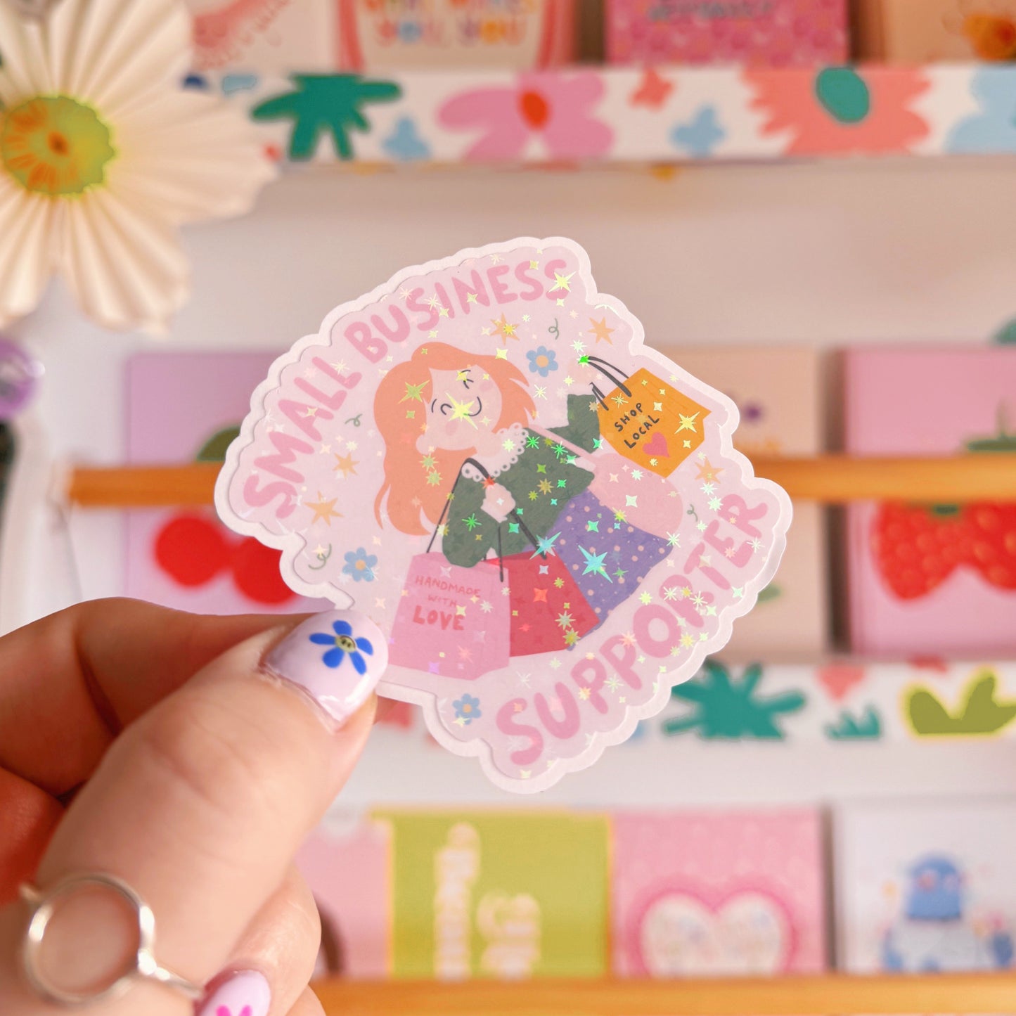 A holographic sticker showing a woman with red hair carrying lots of shopping bags and the words 'small business supporter' around the illustration.