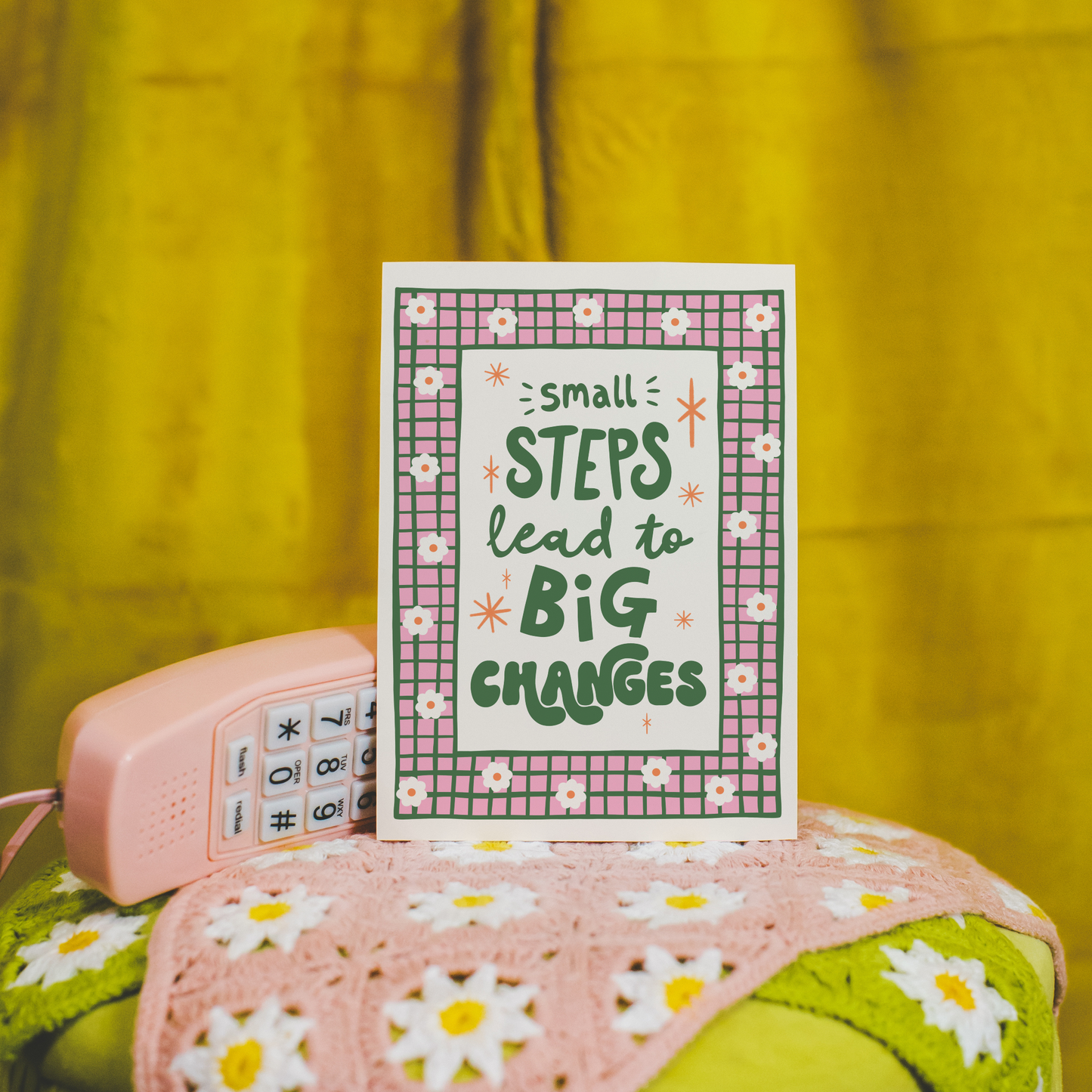 A positive quote print that reads 'small steps lead to big changes' in green hand writing. Around the quote is a hand drawn pink and green checkered border with daisy doodles.