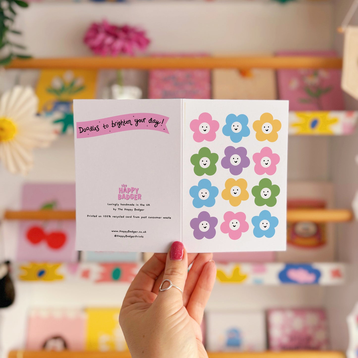 A greetings card with 12 different coloured smiling daisies on the front.