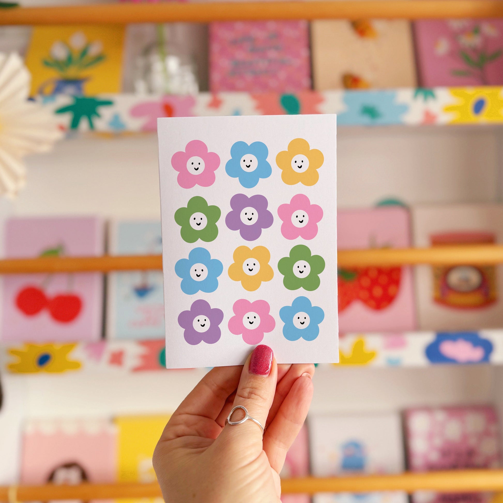 A greetings card with 12 different coloured smiling daisies on the front.