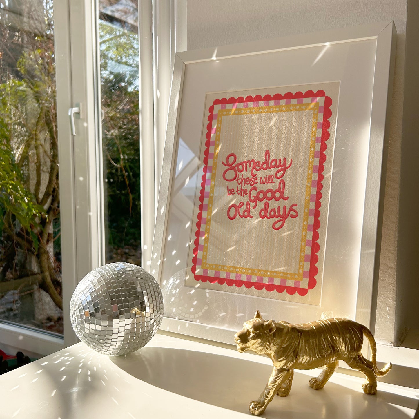 Framed artwork with text, disco ball, and gold cat figurine on a windowsill.