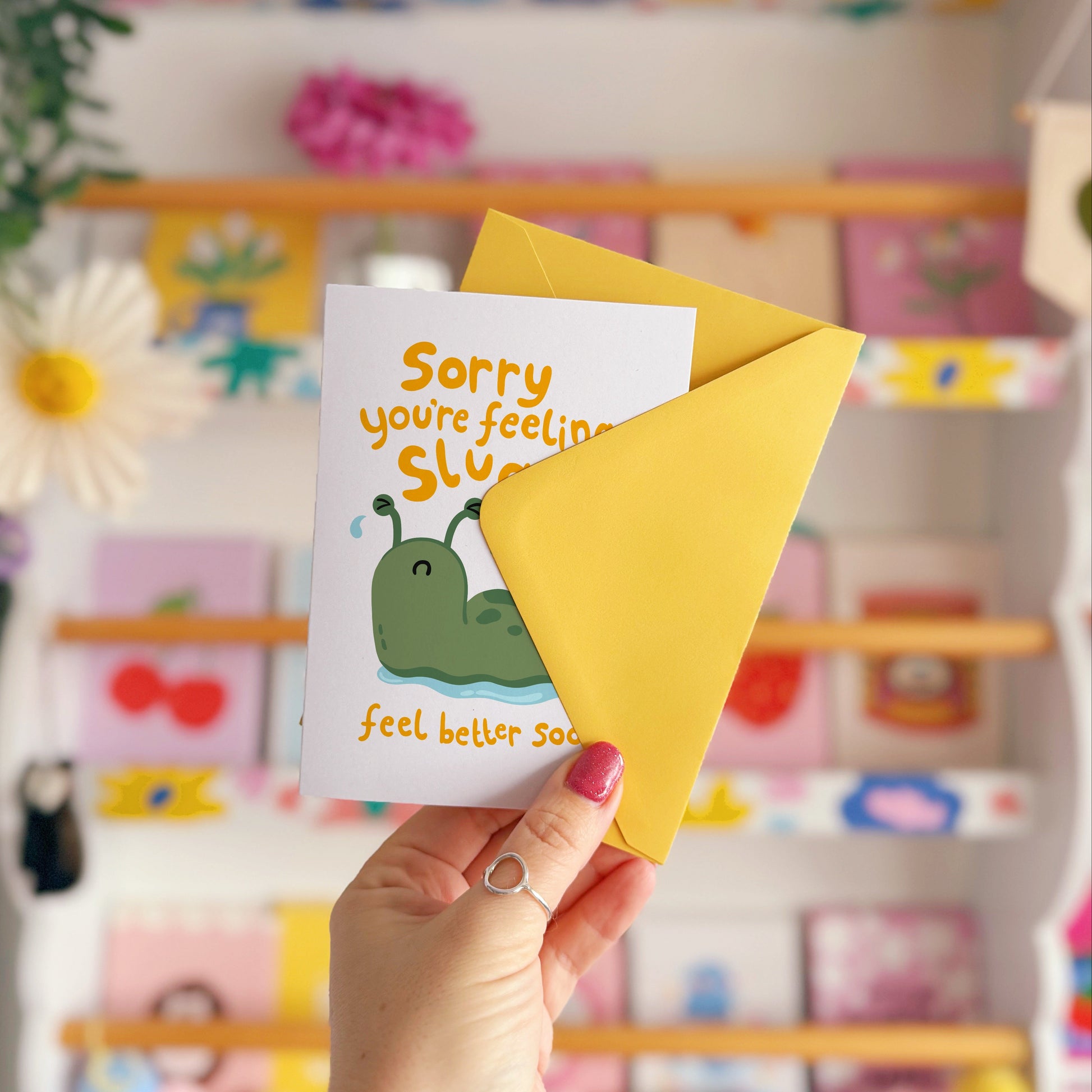 Hand holding a card with a cartoon slug and text 'Sorry, you're feeling sluggish. Feel better soon!'.