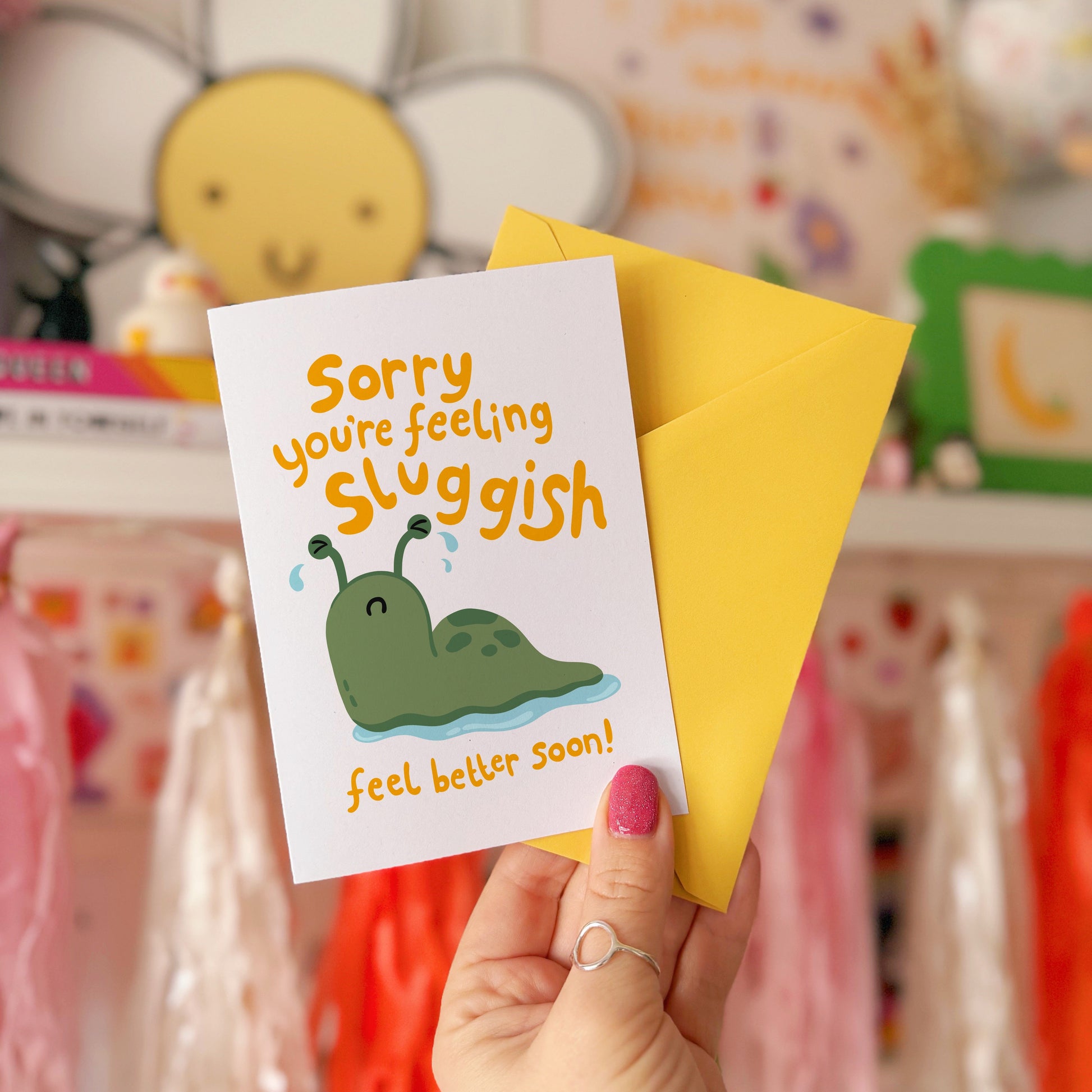 Hand holding a card with a cartoon slug and text 'Sorry, you're feeling sluggish. Feel better soon!'.
