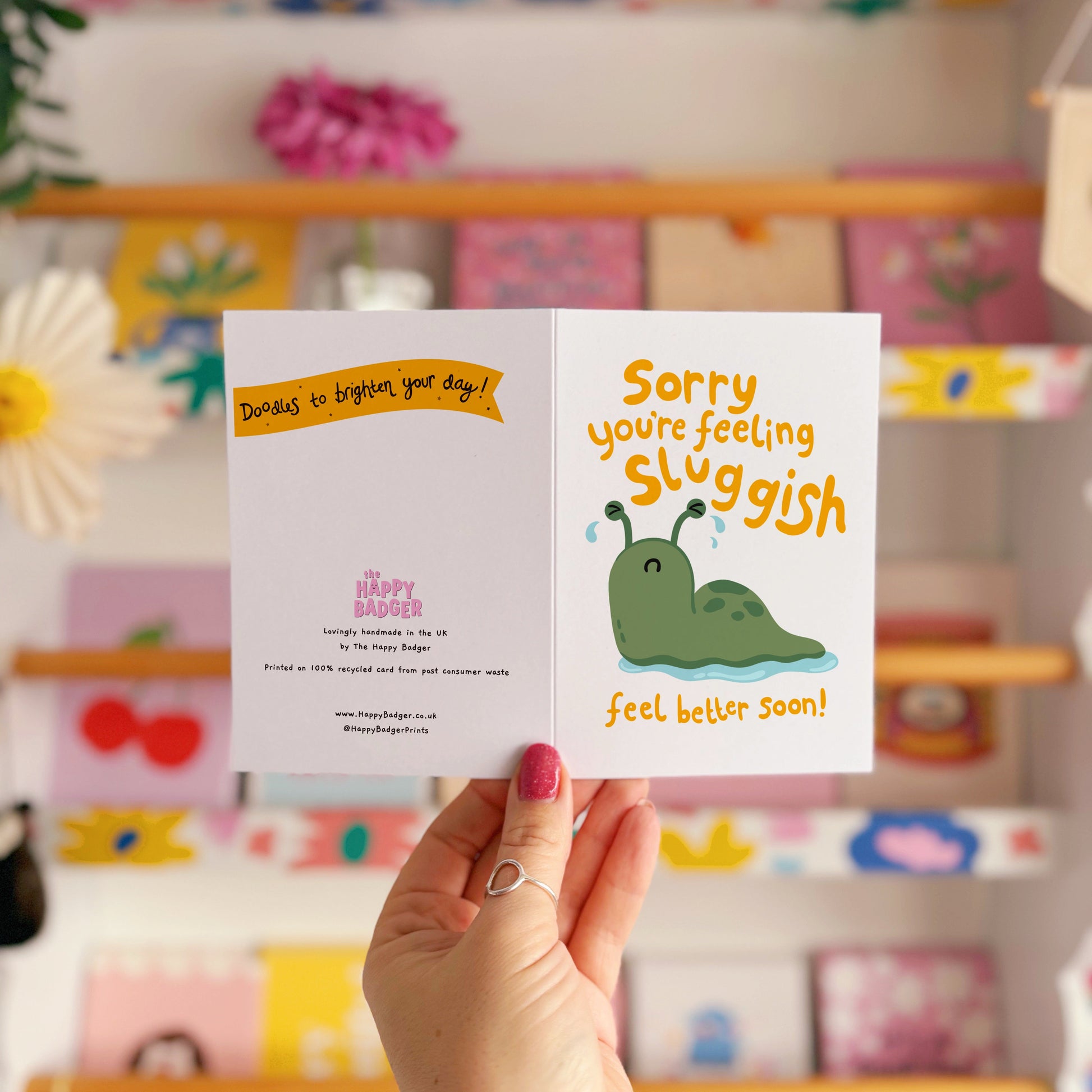 Hand holding a card with a cartoon slug and text 'Sorry, you're feeling sluggish. Feel better soon!'.