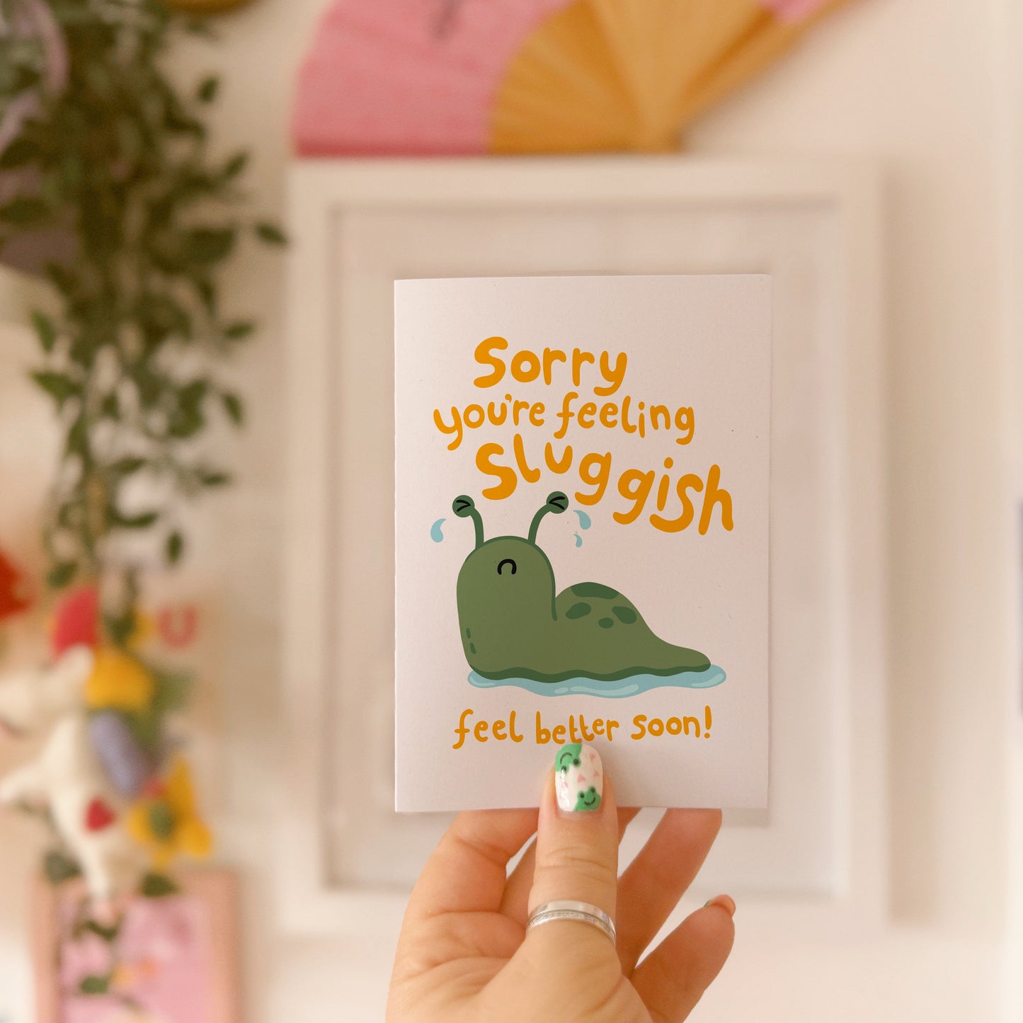 Hand holding a card with a cartoon slug and text 'Sorry, you're feeling sluggish. Feel better soon!'.