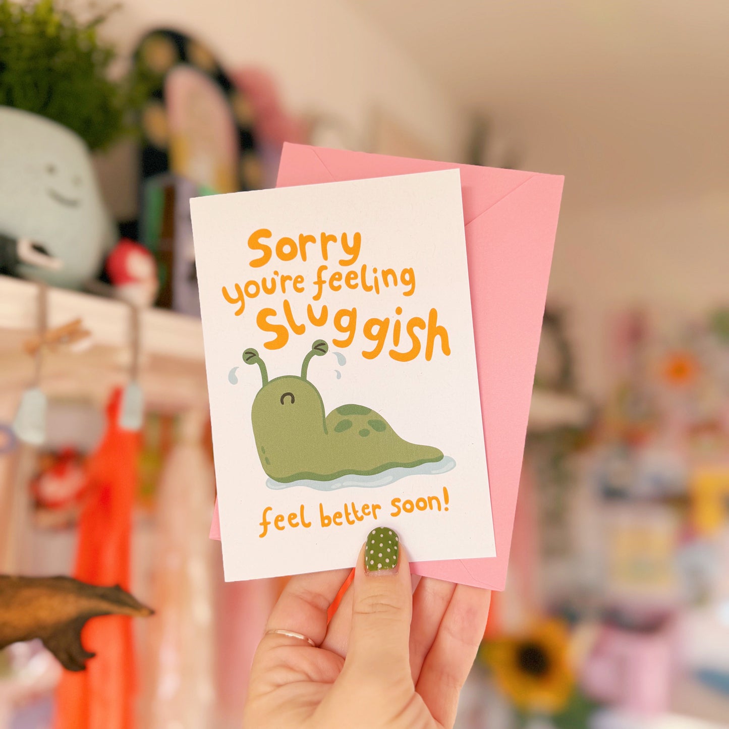 Hand holding a card with a cartoon snail and text 'Sorry you're feeling sluggish. Feel better soon!'.