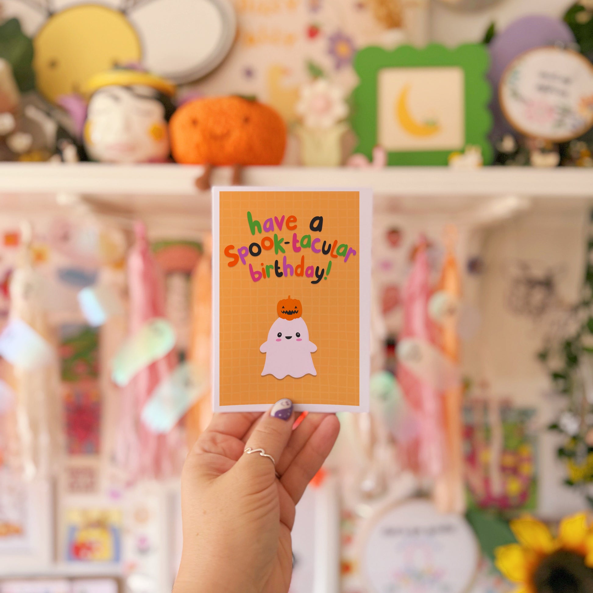 Hand holding a Halloween-themed card with text and graphics against a colorful background.