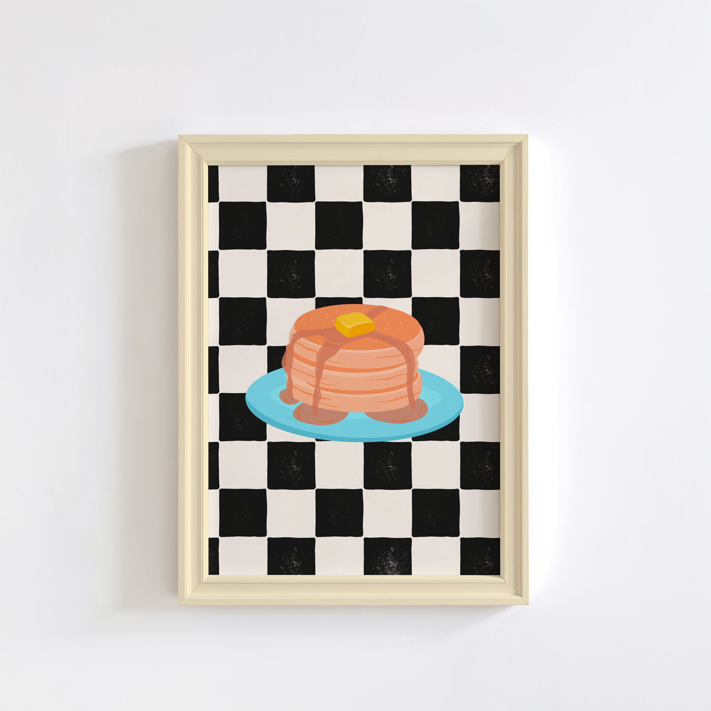 A framed art print featuring a black and white checkered pattern with a colourful illustration of pancakes on a blue plate.