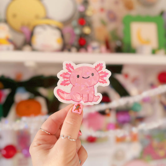 Hand holding a pink axolotl sticker with a colorful blurred background