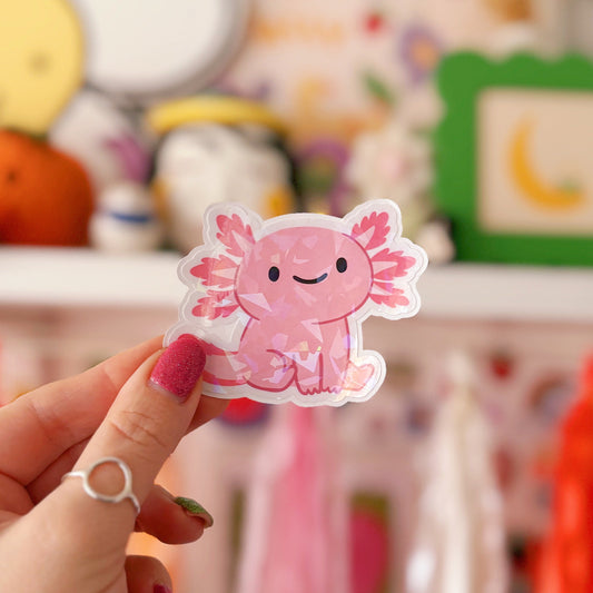 Hand holding a pink axolotl sticker in front of a colourful background