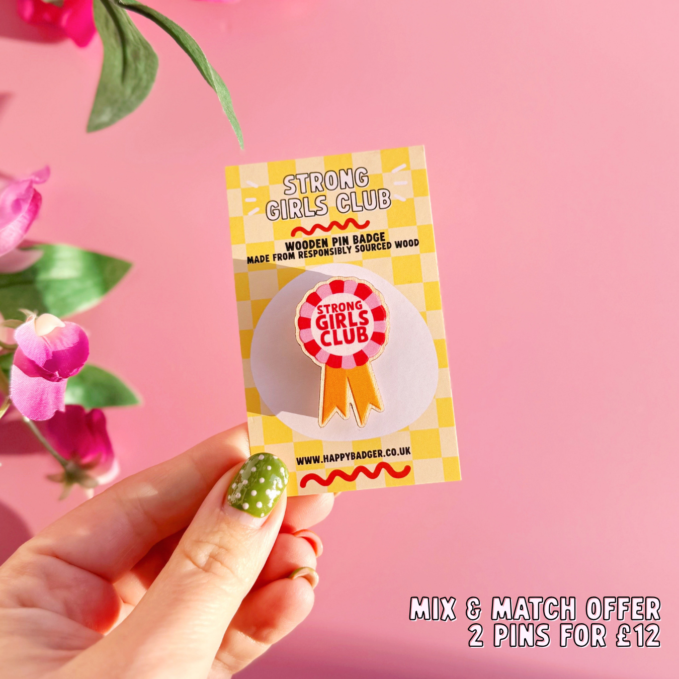 A wooden pin badge, in the shape of a rosette, that says 'strong girls club' in the centre. The colours are red, pink and golden yellow.