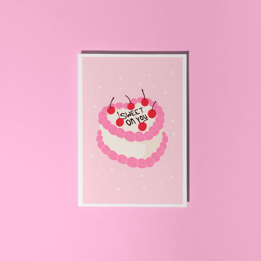 A pink love themed card, with a cake illustration. There is black icing on the cake says 'sweet on you' and the rest of the cake has cherries and pink and white icing.