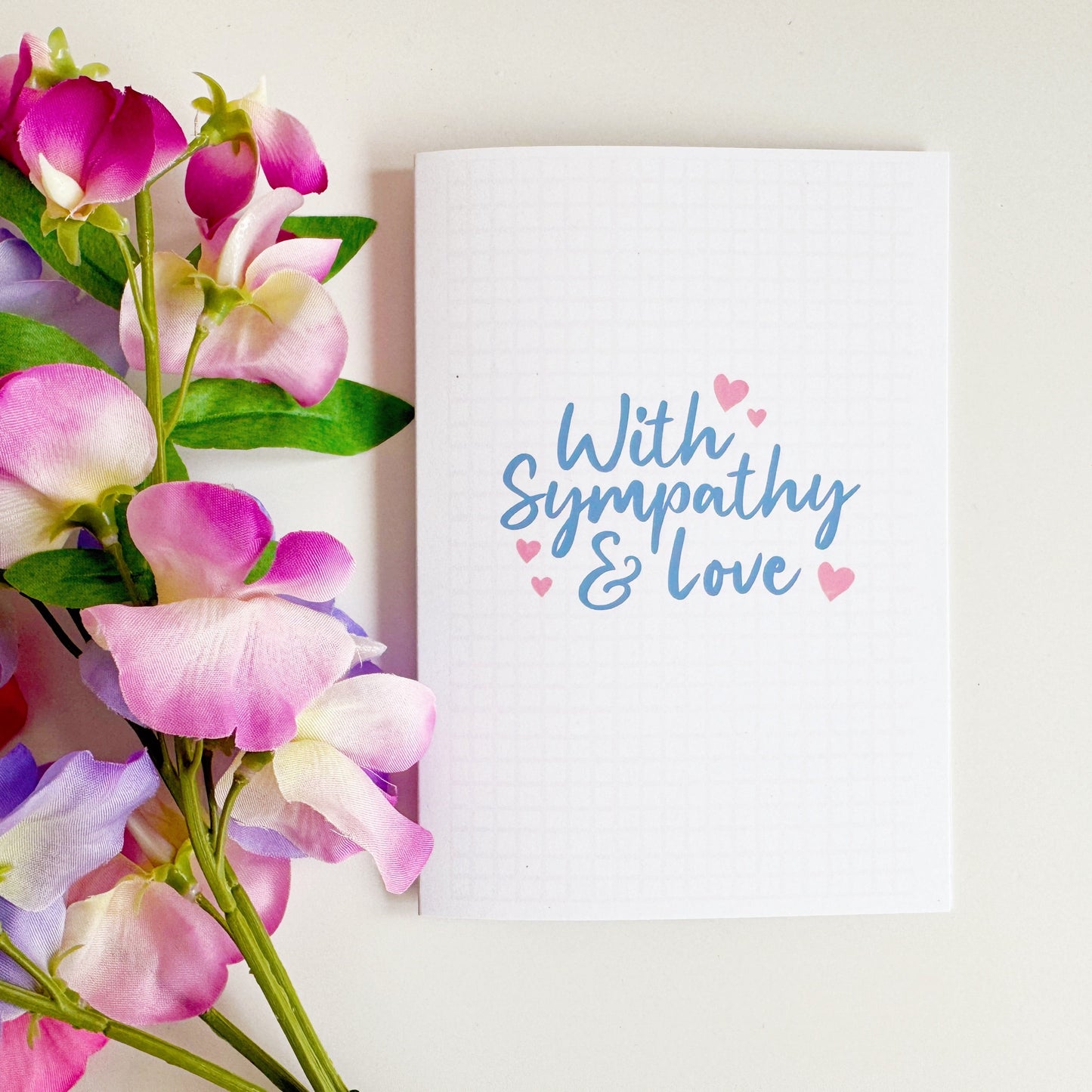 A simple card, with the words with sympathy and love in a blue script font surrounded by small pink hearts.