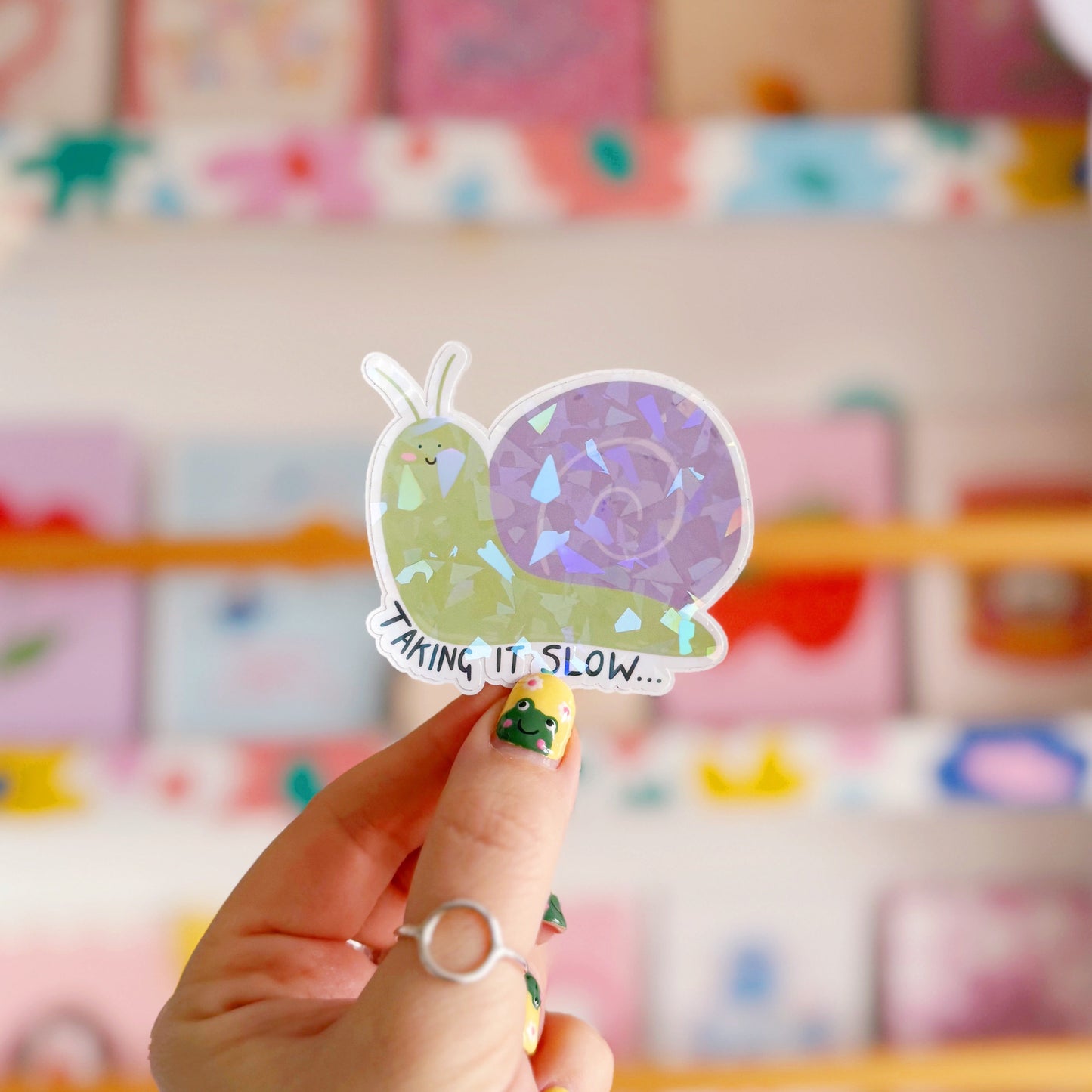 A holographic sticker of a purple and green smiling snail, with text underneath that reads 'taking it slow.'