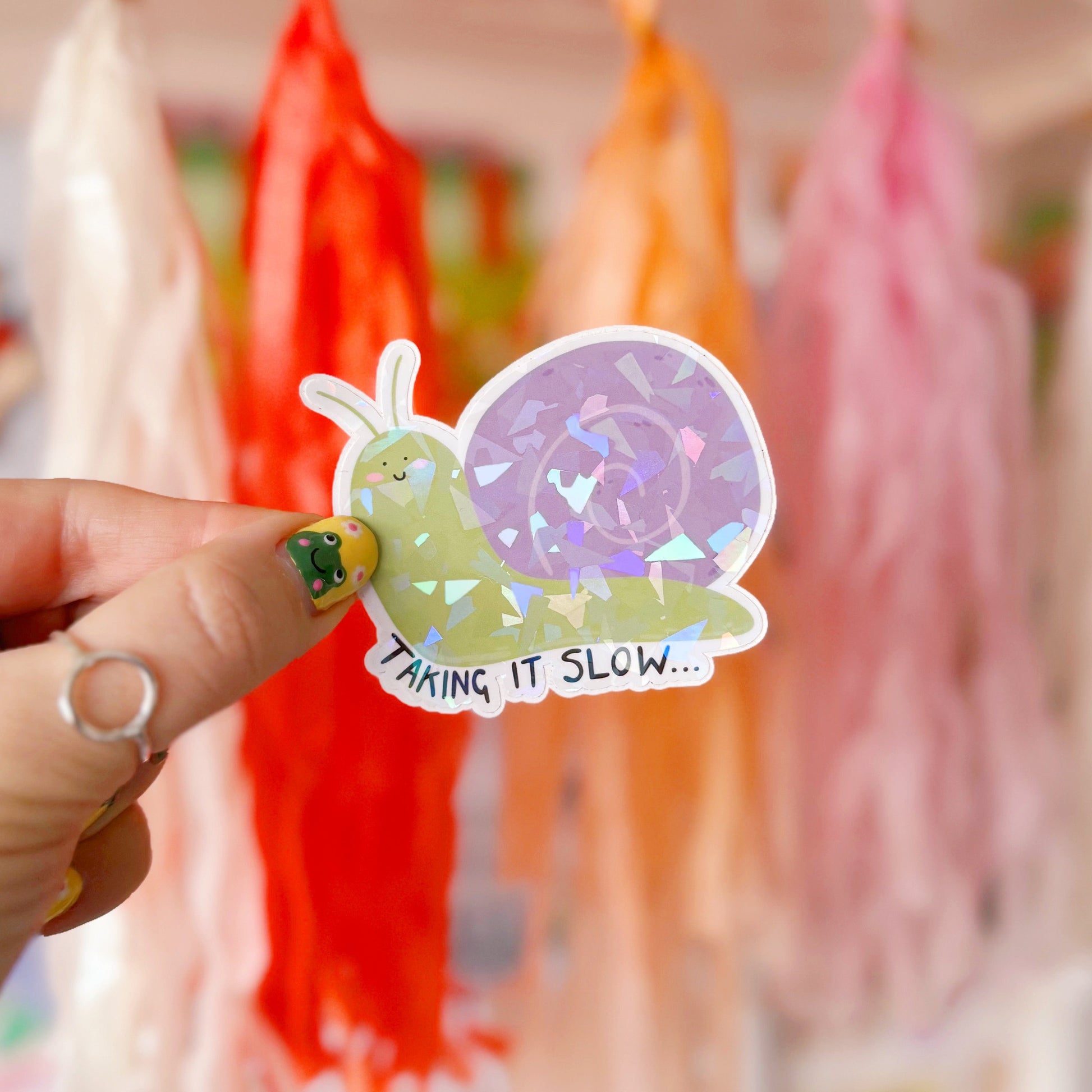 A holographic sticker of a purple and green smiling snail, with text underneath that reads 'taking it slow.'