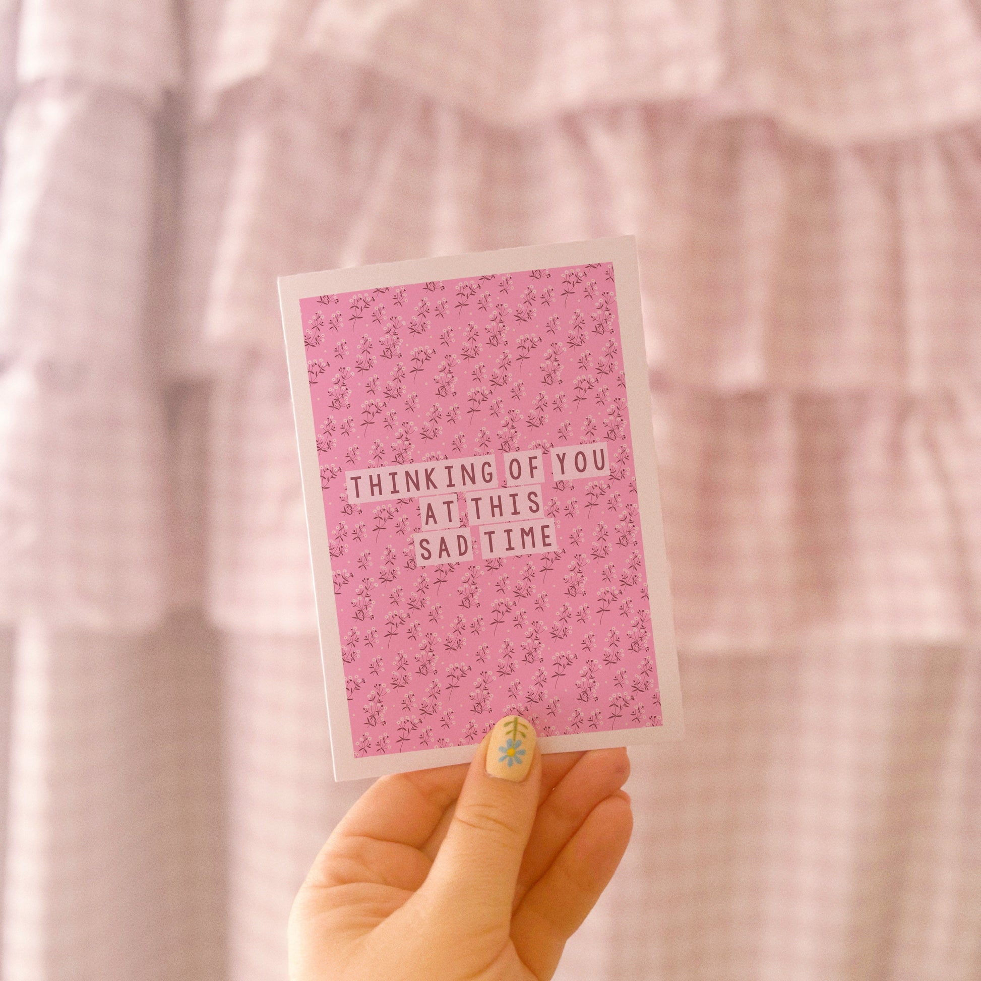 A card with a pink floral patterned background, and the words 'thinking of you at this sad time' in the centre.