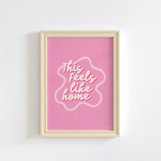 A pink print, shown in a frame, with white text that reads 'this feels like home'.