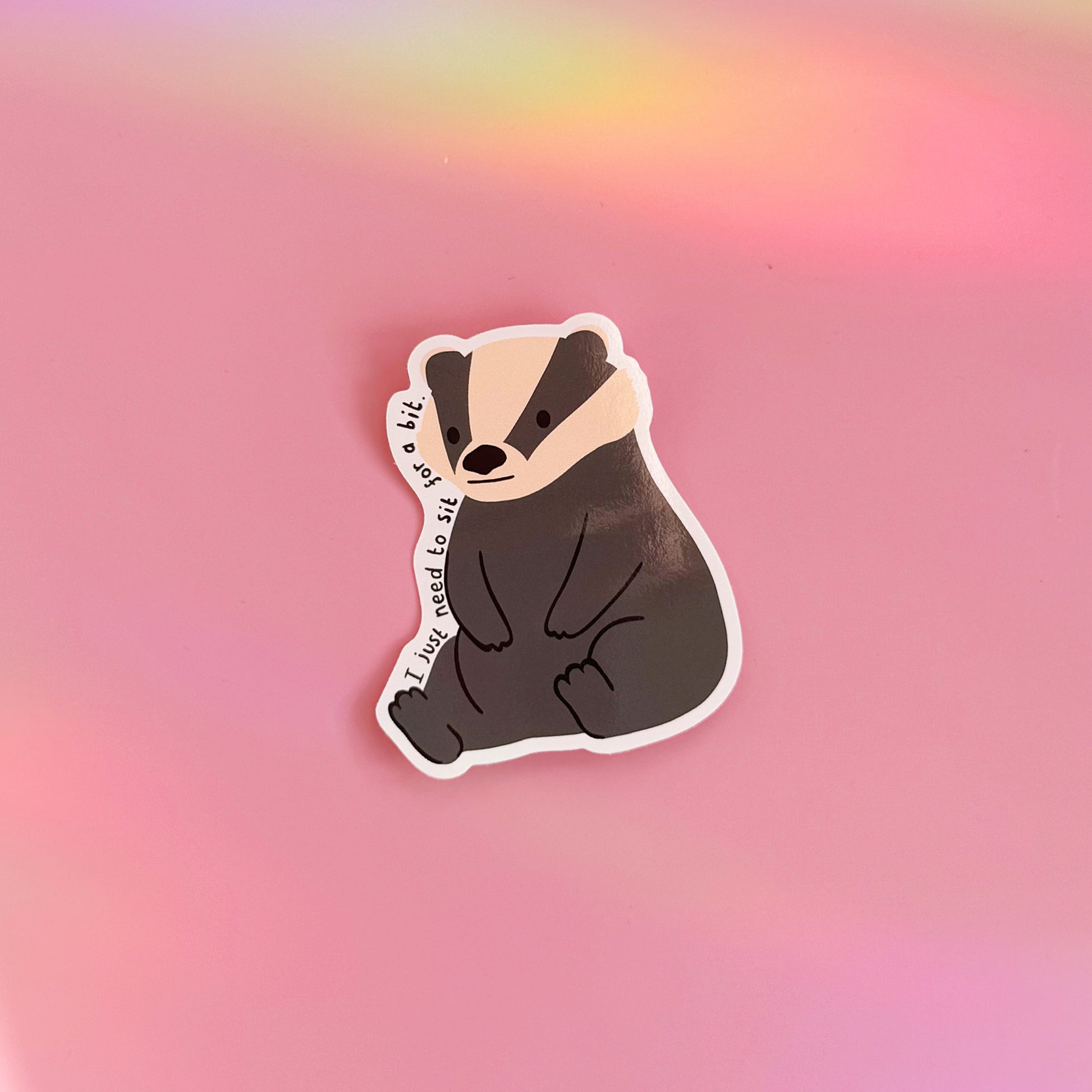A waterproof vinyl sticker featuring a badger illustration, and text that reads 'I just need to sit for a bit'.