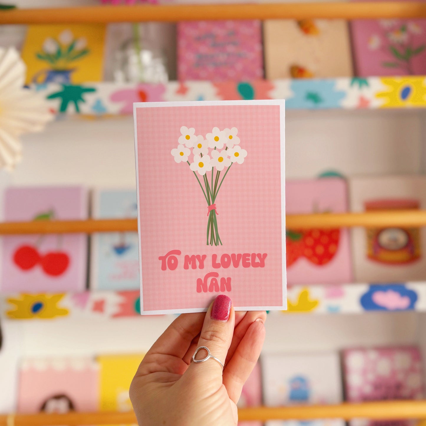 A pink greeting card with the words 'to my lovely nan' on the front, with a bunch of daisies.