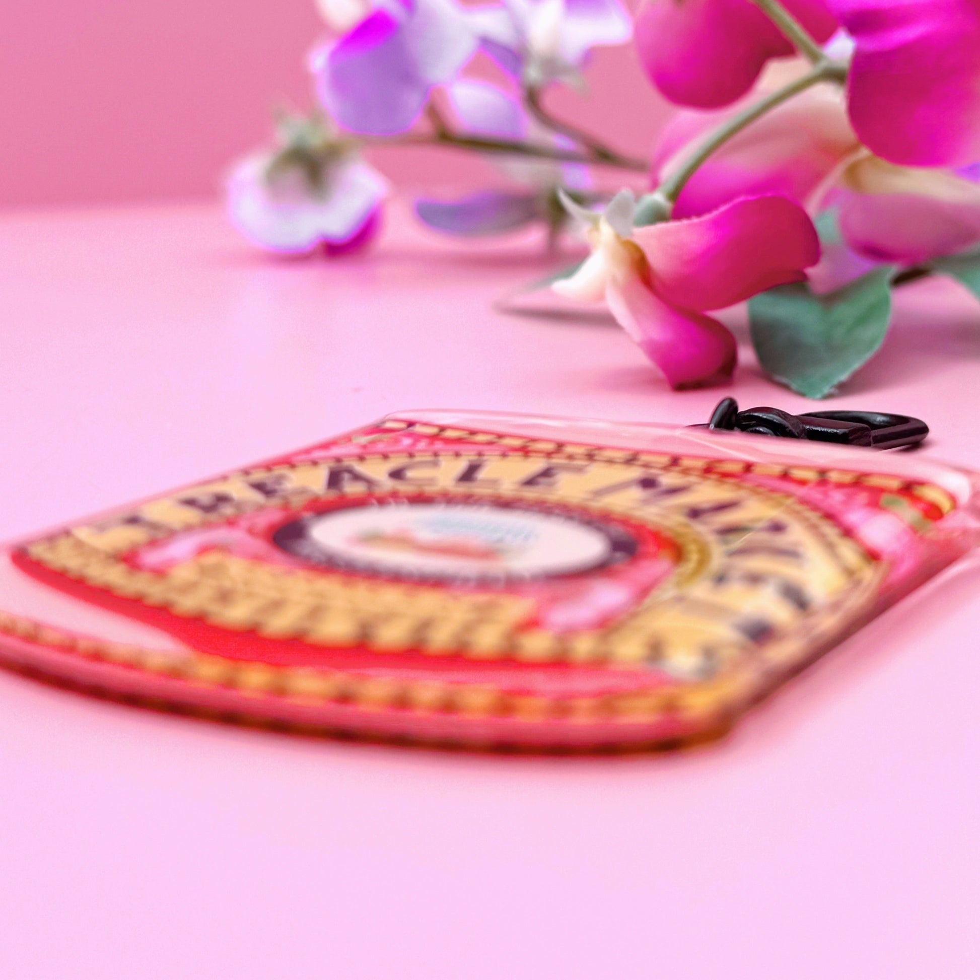 A Treacle Market tin keyring against a pink background with flowers.
