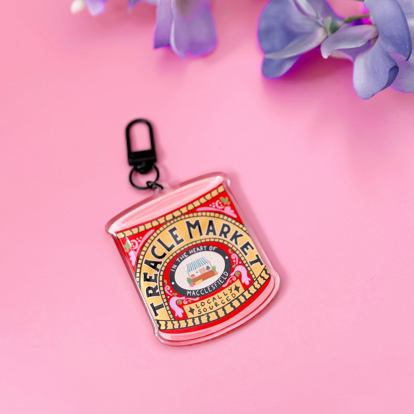A Treacle Market tin keyring against a pink background with flowers.