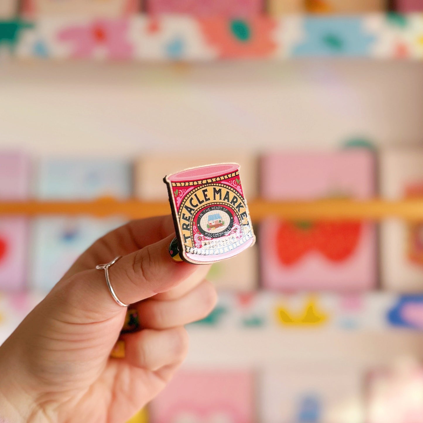 A wooden pin badge, with a glossy finish. The artwork is of a tin of treacle, but says 'treacle market' after the monthly market in Macclesfield.