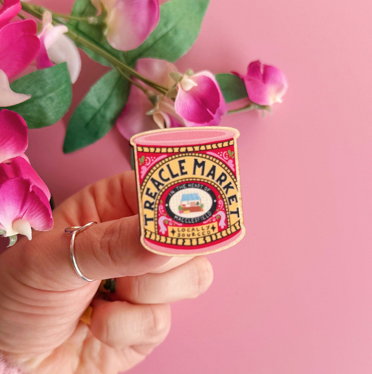 A wooden pin badge, with a glossy finish. The artwork is of a tin of treacle, but says 'treacle market' after the monthly market in Macclesfield.