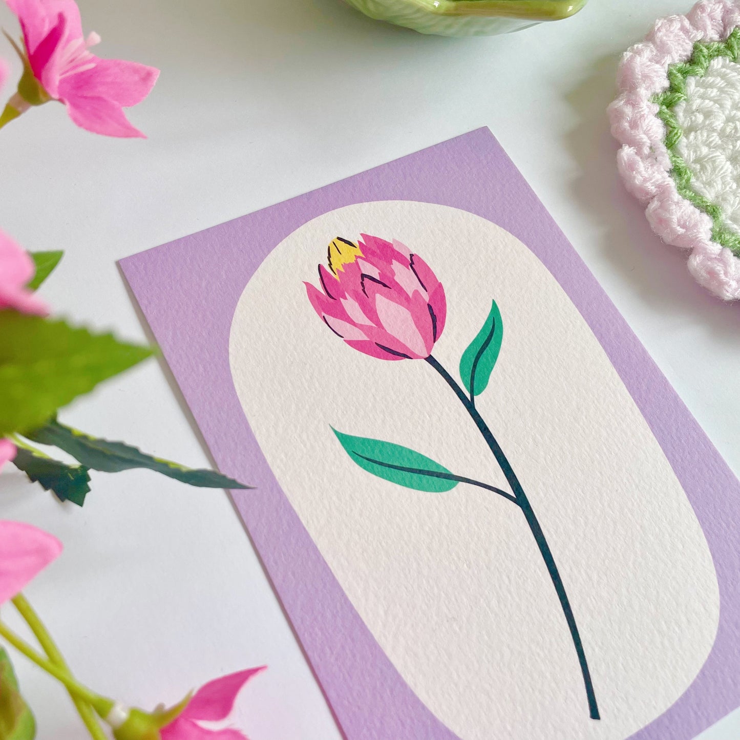 An illustration of a tulip stem, with a purple frame printed onto a textured postcard.