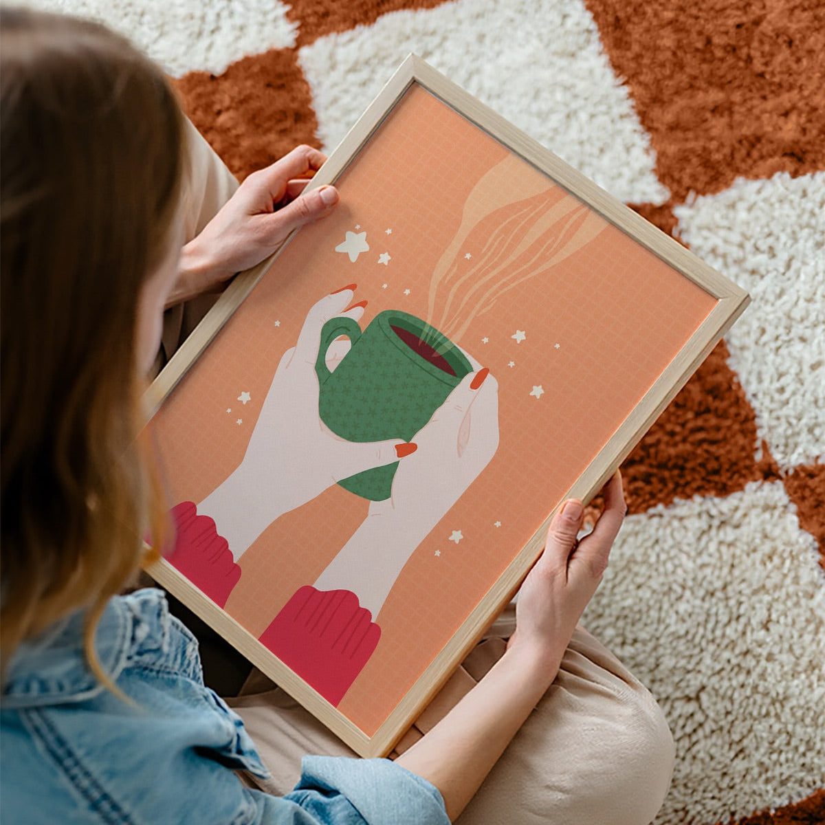 An illustration of a pair of woman's hands holding a green patterned mug, with coffee in. The print background is orange and there are little white stars around the illustration.
