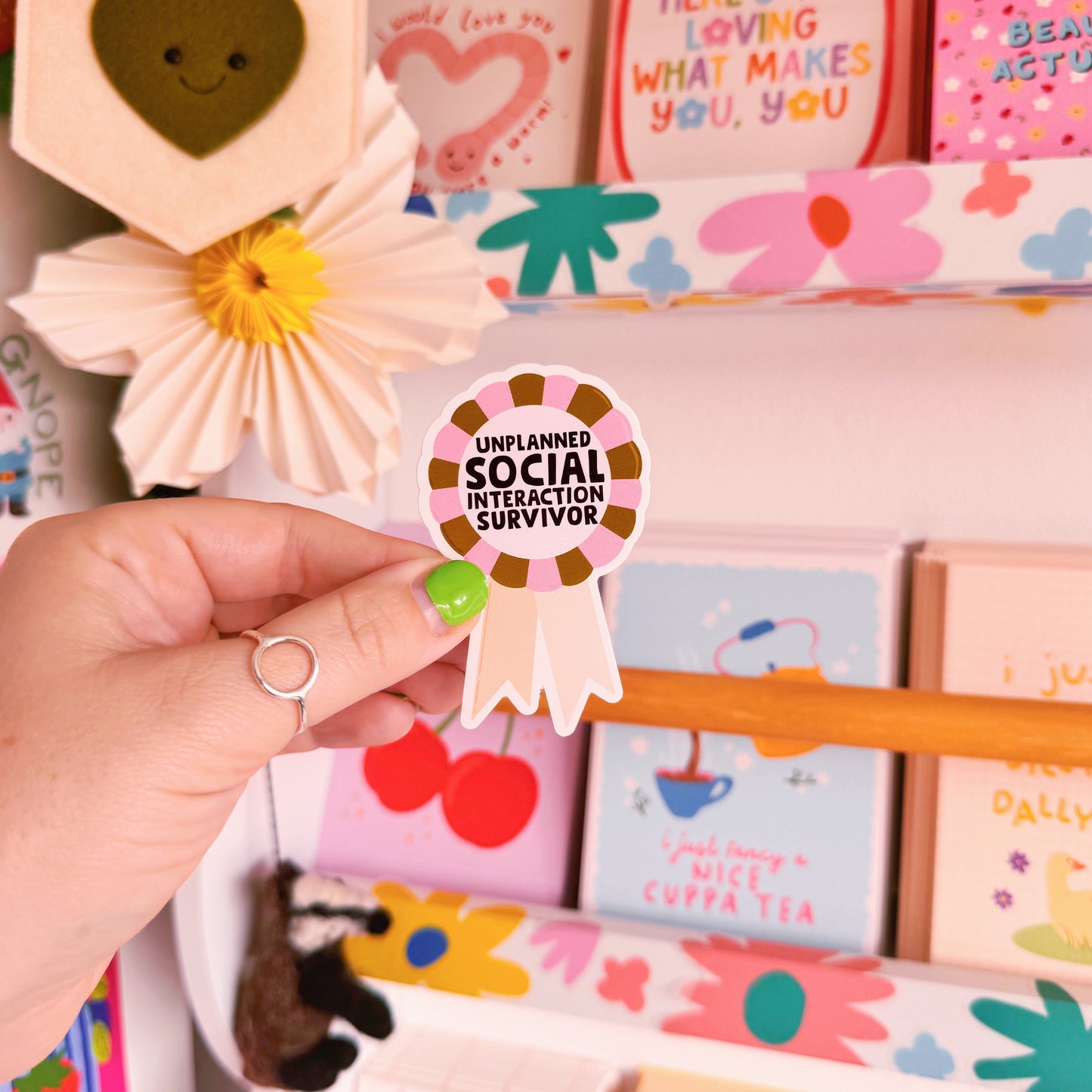 A waterproof vinyl sticker featuring an illustration of an award rosette, with the words 'unplanned social interaction survivor' in the centre.