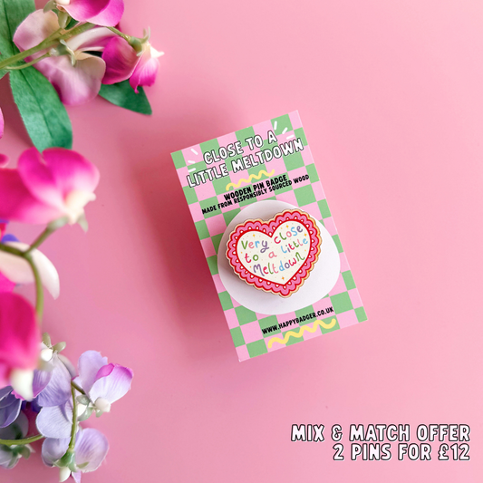 A wooden pin badge, with a glossy finish, in the shape of a heart with a funny quote in the centre.