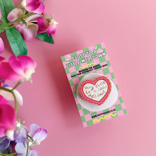 A wooden pin badge, with a glossy finish, in the shape of a heart with a funny quote in the centre.