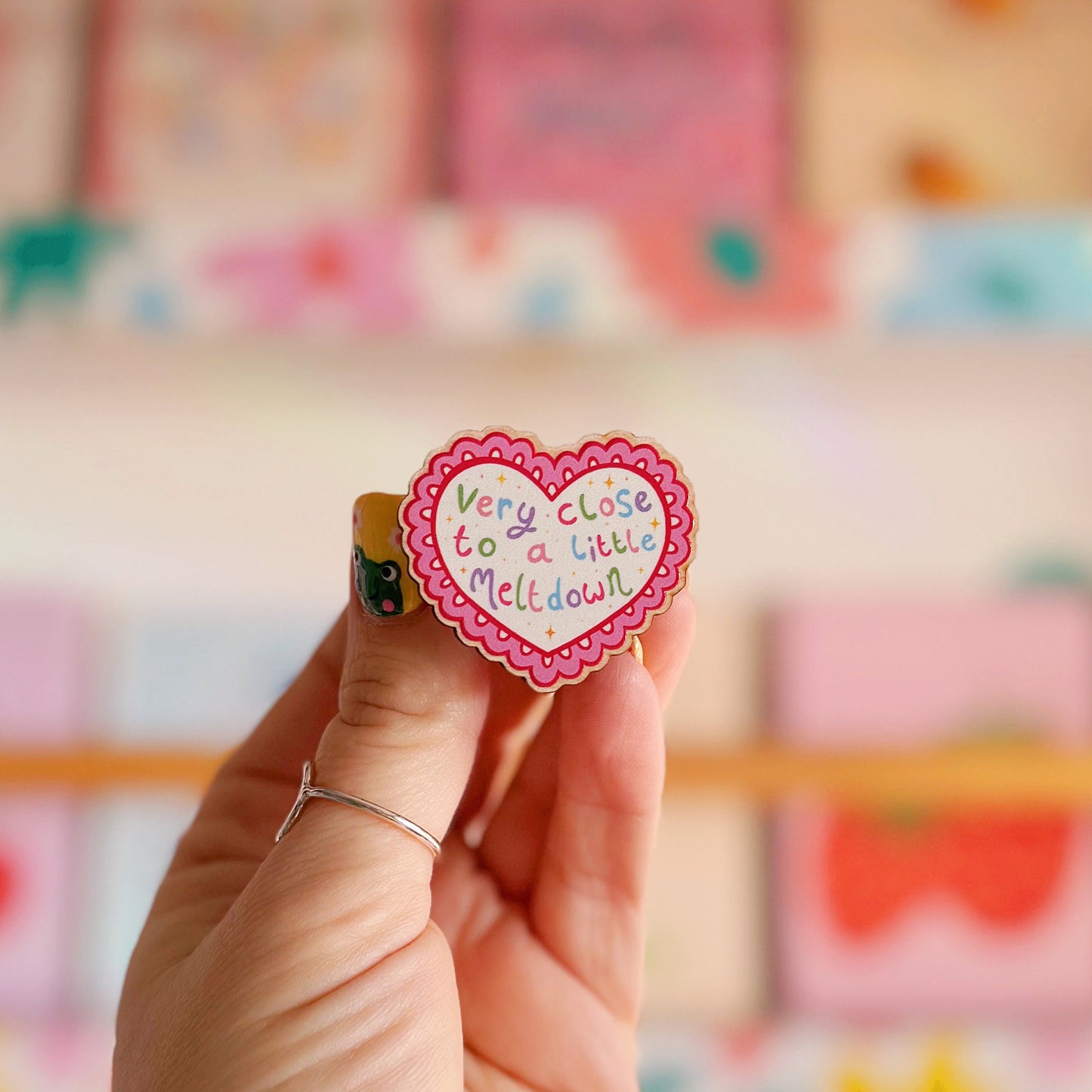 A wooden pin badge, with a glossy finish, in the shape of a heart with a funny quote in the centre.