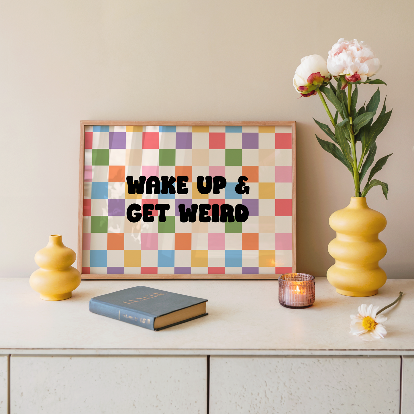 Decorative shelf with a colorful checkered wall art print, book, candle, and flowers.